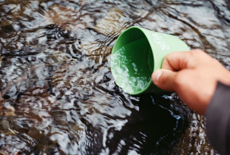 Person using a cup to fetch water in a stream. Survive, Survival